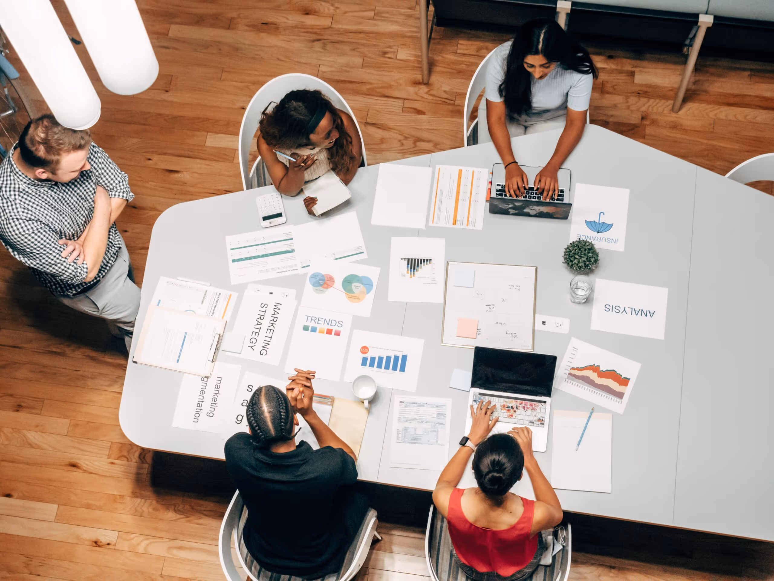 Four colleagues collaborate around a table with laptops, papers, and marketing strategy charts.